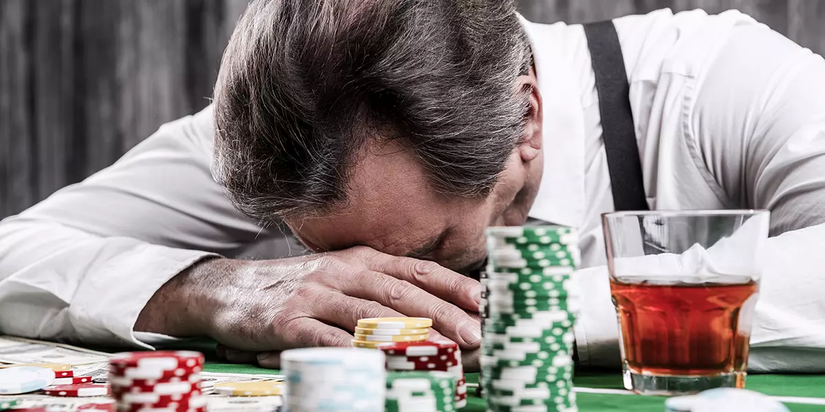 Frustrierter Mann mit alkoholischem Getränk neben sich legt Kopf auf den Casino Tisch
