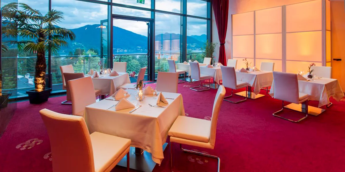 Elegant gedeckte Restaurant-Tische vor Panoramafenster mit Aussicht auf die Berge