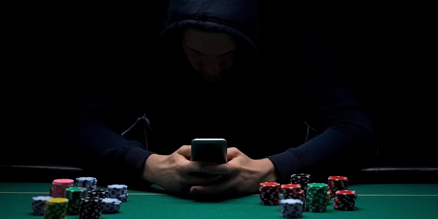 Vermummter Spieler am Pokertisch mit Chip-Stapeln vor sich liegend