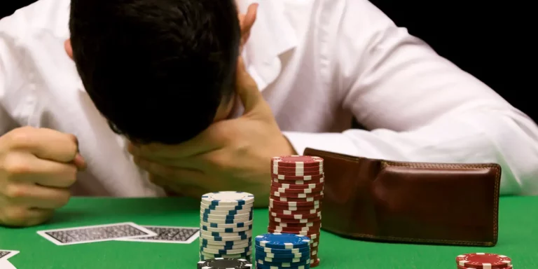 Verzweifelter Mann stützt Kopf auf Pokertisch auf neben Pokerchips und ausgeklapptem Portmonee