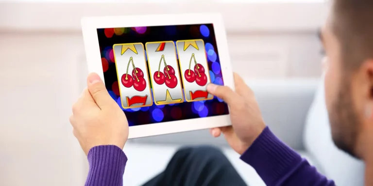 Mann hält Tablet in den Händen, auf dem ein Online-Slot läuft