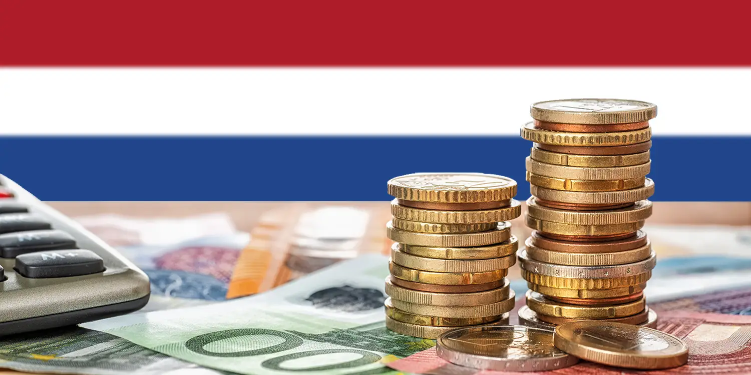 Münzstapel und Geldscheine auf Tisch mit niederländischer Flagge im Hintergrund