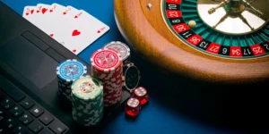 Laptop neben Pokerchips, Spielkarten, Würfeln und Roulette-Kessel