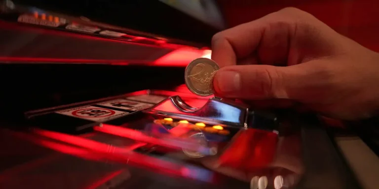 Hand eines Spielers wirft 2 Euro Münze in einen Spielautomaten