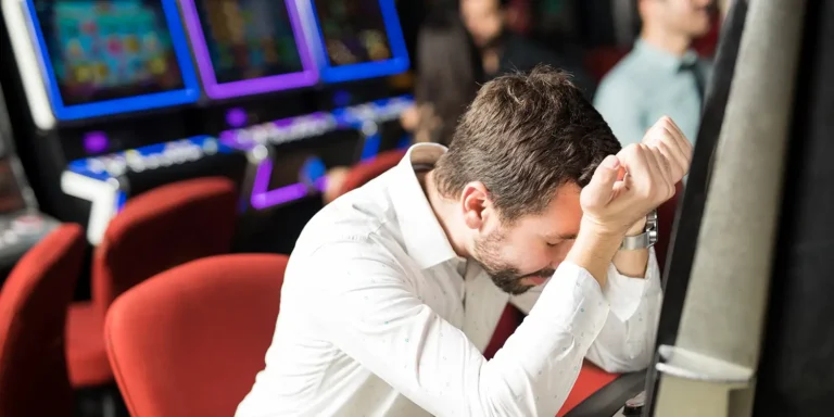 Mann stützt frustriert seinen Kopf auf die Hände beim Spielen an einem Automaten