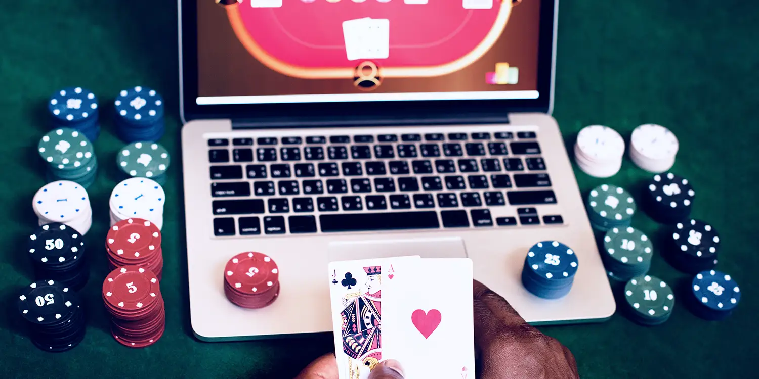 Spieler mit Spielkarten und Pokerchips vor Laptop, auf dem Online-Poker läuft.