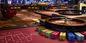 Großer Saal mit mehreren Roulette-Tischen und vielen Spielautomaten im Hintergrund