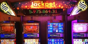 4 Spielautomaten nebeneinander und Anzeigetafel mit Stand des aktuellen Jackpots darüber